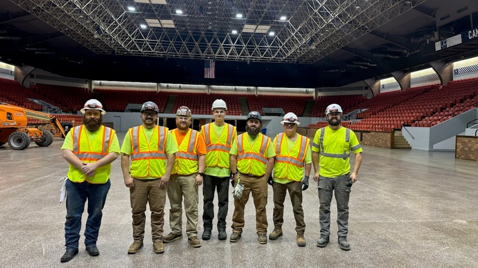 Men with hard hats and yellow safety shirts/vests in a stadium