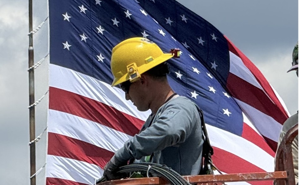 Man with a yellow hard hat next to an American Flag