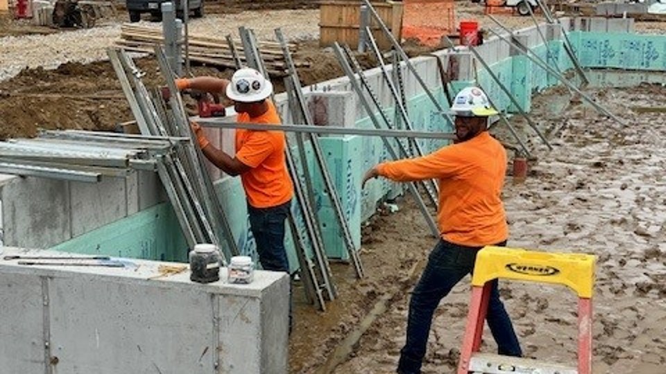 Two men in orange with hard hats at a job site under construction